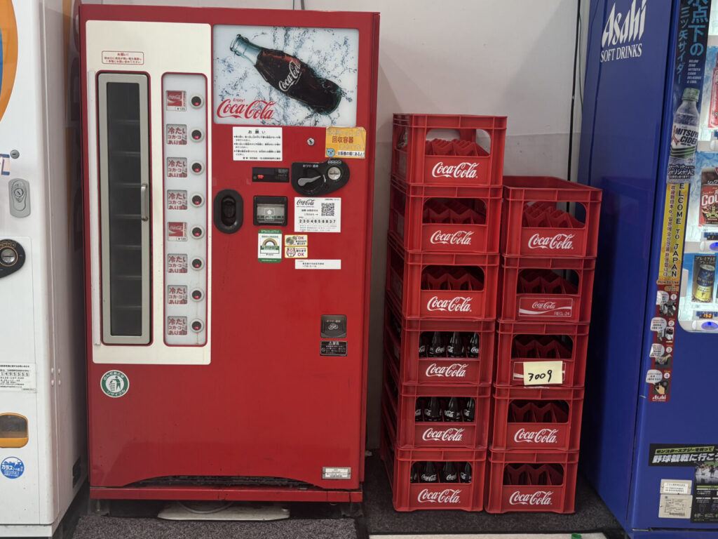 瓶コーラの自販機の隣に積まれた瓶コーラのケース