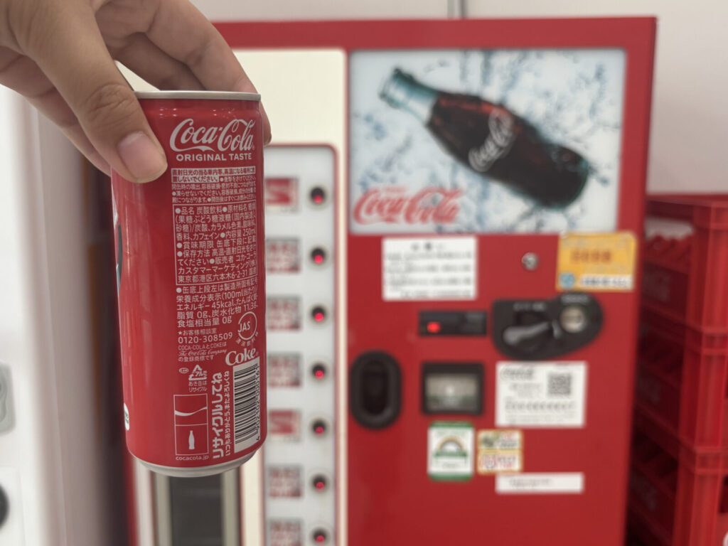 瓶コーラの自販機を背景にした缶コーラの写真